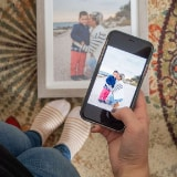 Person viewing a photo of two people on a beach on their smartphone, with a framed photo nearby